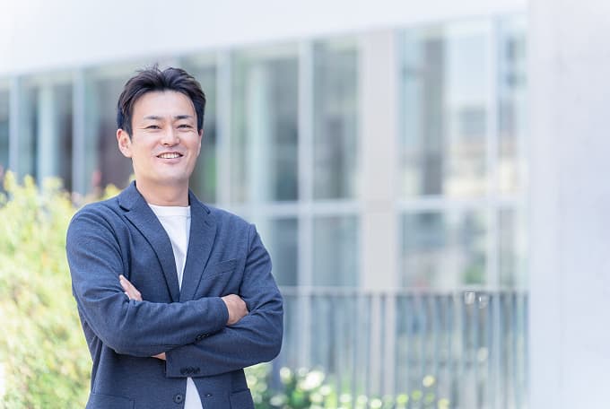 企業の前で腕を組み、笑顔を見せる代表取締役社長のポートレート